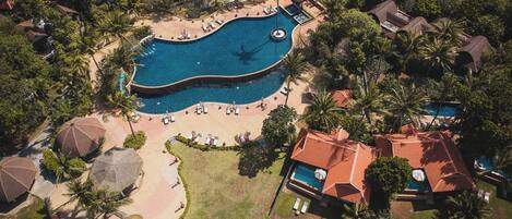 Vista aerea di un resort con una grande piscina, lettini prendisole e palme.