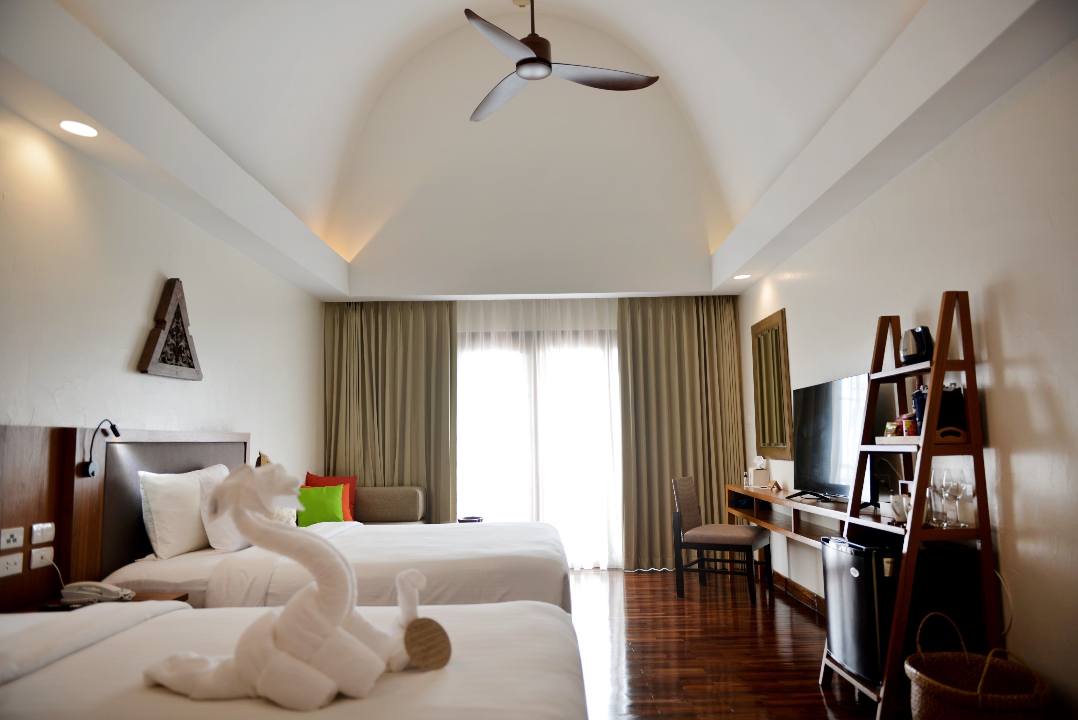 A hotel room with two beds, a ceiling fan, a TV, a desk, and a chair.