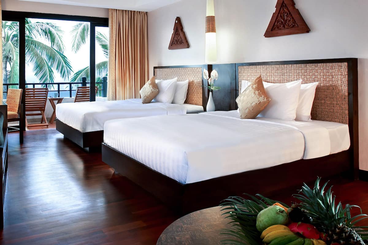 A hotel room with two beds, a balcony with a view of palm trees, and a dining area with a table and chairs.