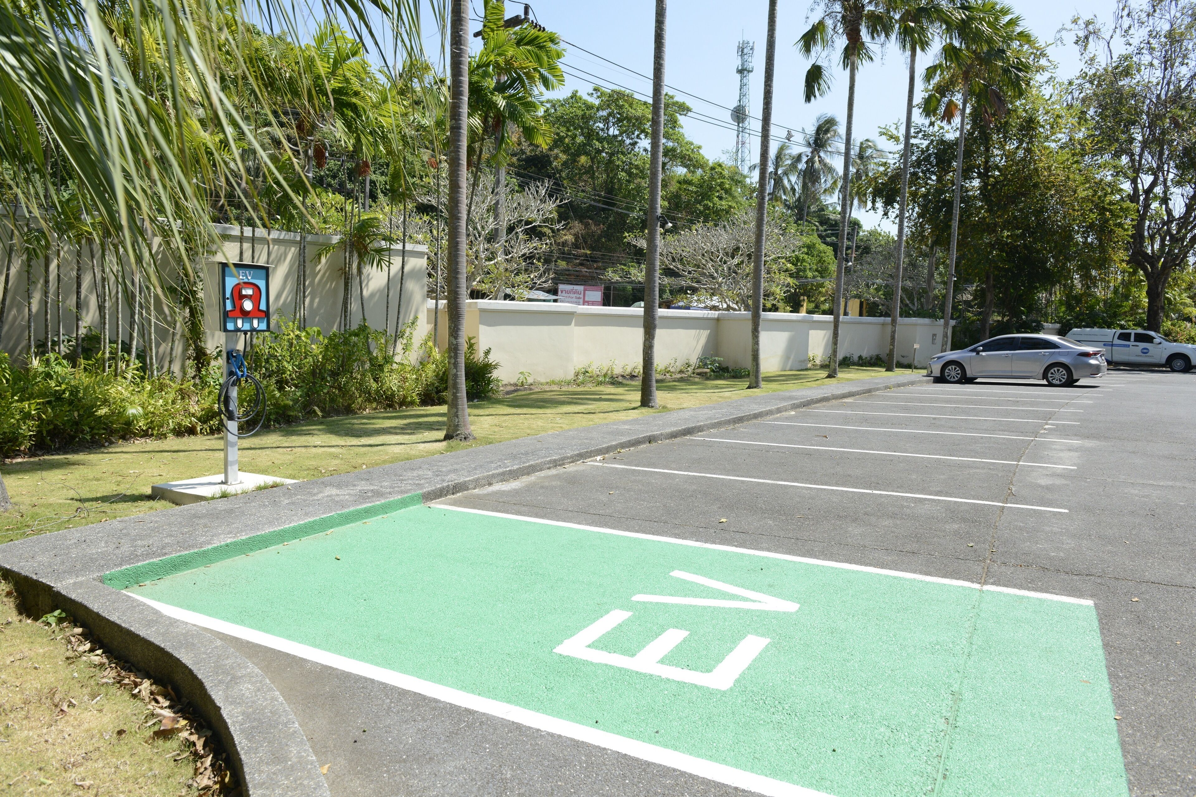 Un parking doté d’une borne de recharge pour véhicules électriques, peinte en vert, et d’un panneau indiquant une zone où le stationnement est interdit.