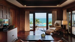 A spacious room with a wooden floor, a ceiling fan, a television, a dining table, and a view of the ocean through large windows. - Rawi Warin Resort and Spa (Ko Lanta)