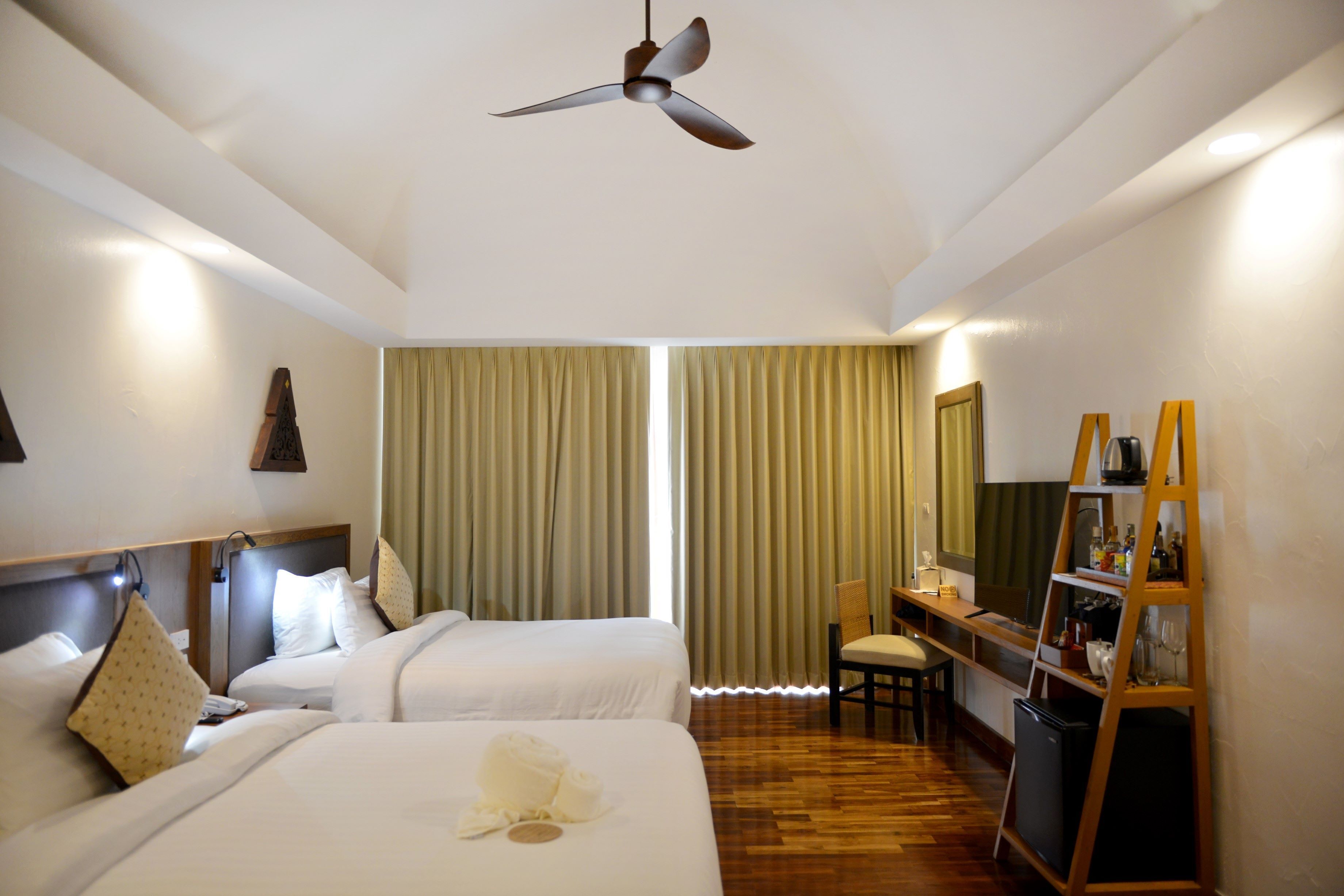 Habitación de hotel con dos camas, un escritorio, una silla, un televisor y un ventilador de techo.