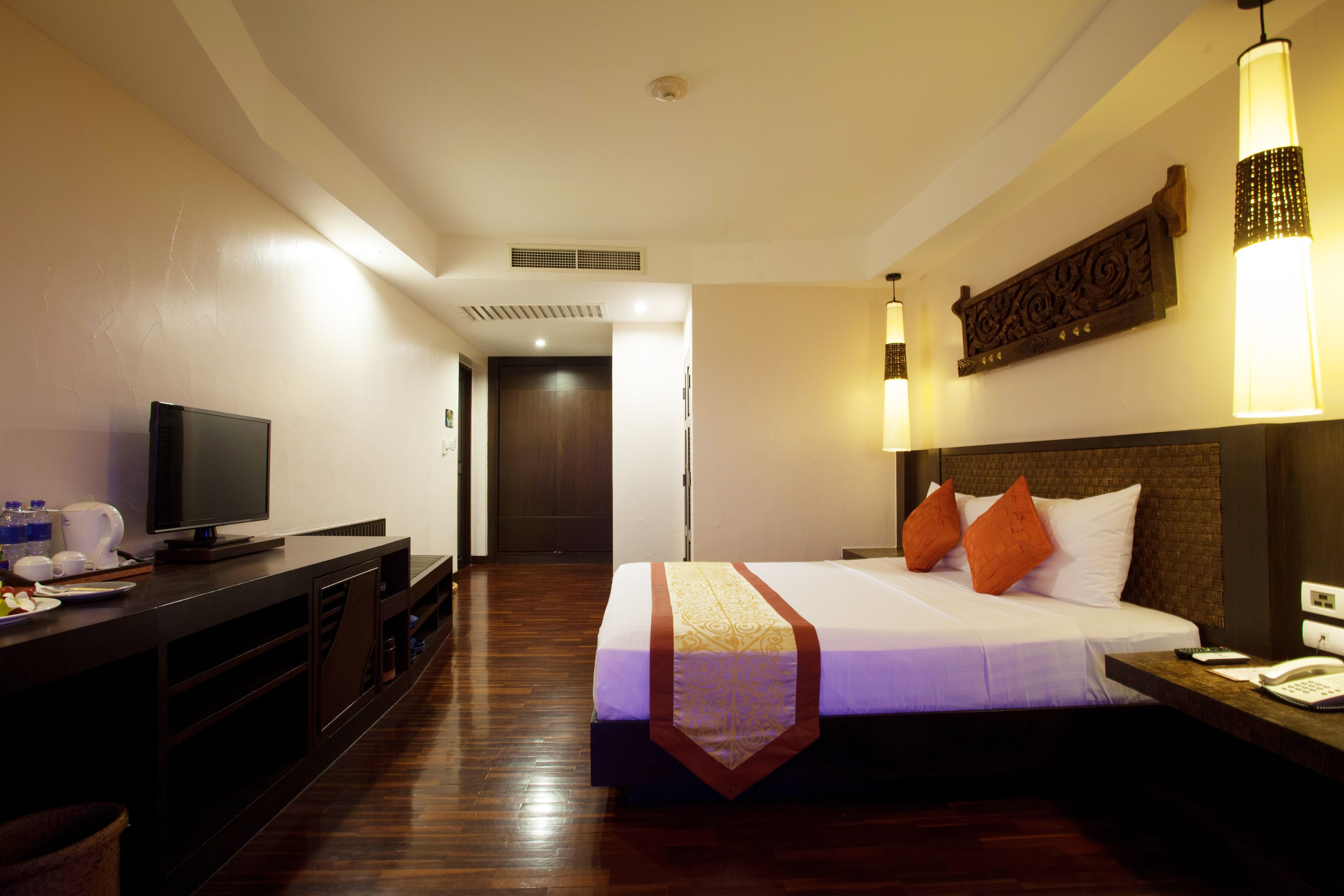 Quarto de hotel com cama, mesa de cabeceira, luminária e televisão sobre um aparador.