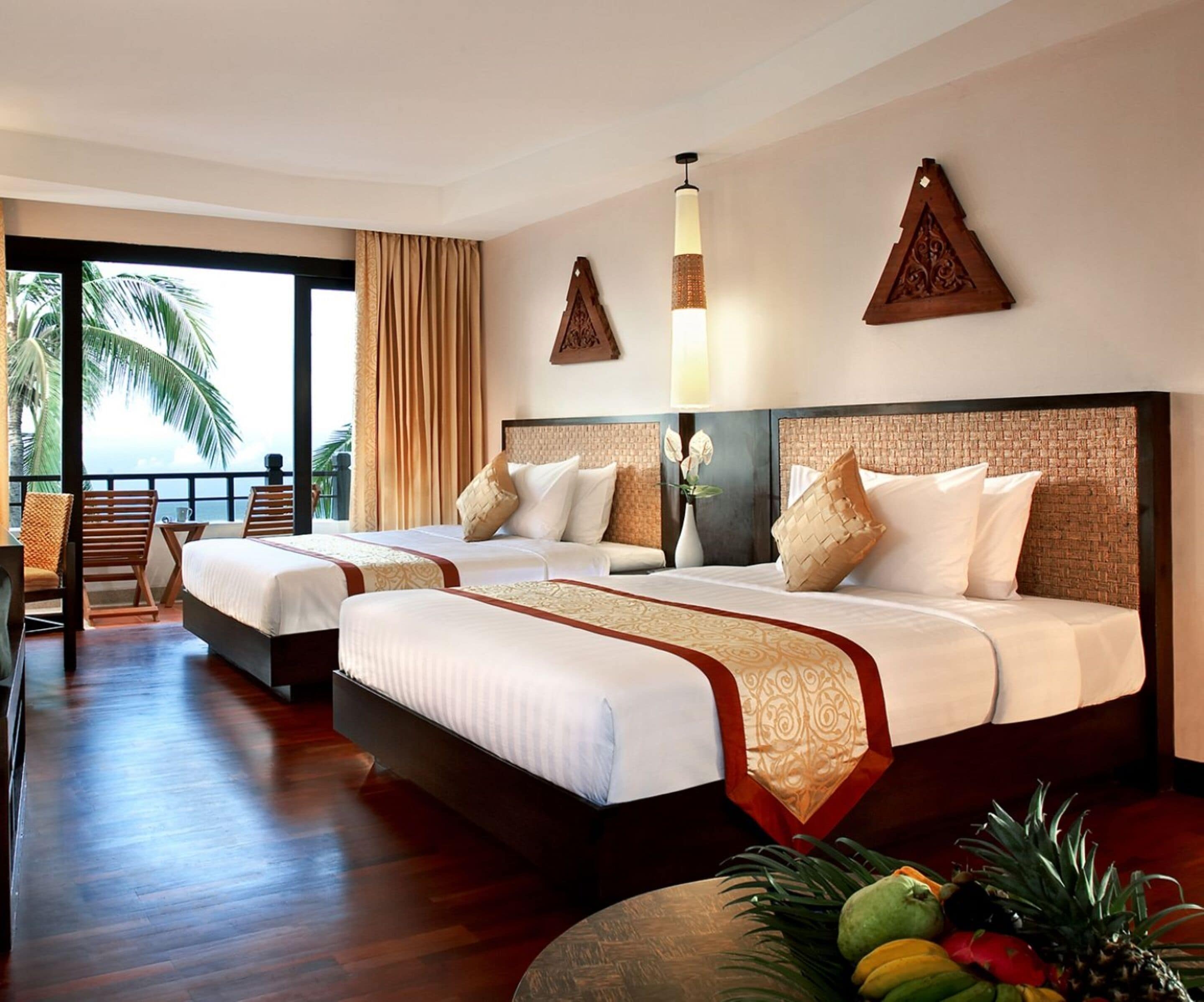 Habitación de hotel con dos camas, un balcón con vistas y un frutero en el suelo.