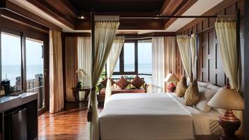 A spacious bedroom with a large bed, a bedside table with a lamp, and a view of the ocean through large windows.