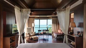 Ein geräumiges Schlafzimmer mit einem großen Bett, einem Fernseher, einer Sitzecke mit Tisch und Stühlen und Meerblick durch große Fenster.