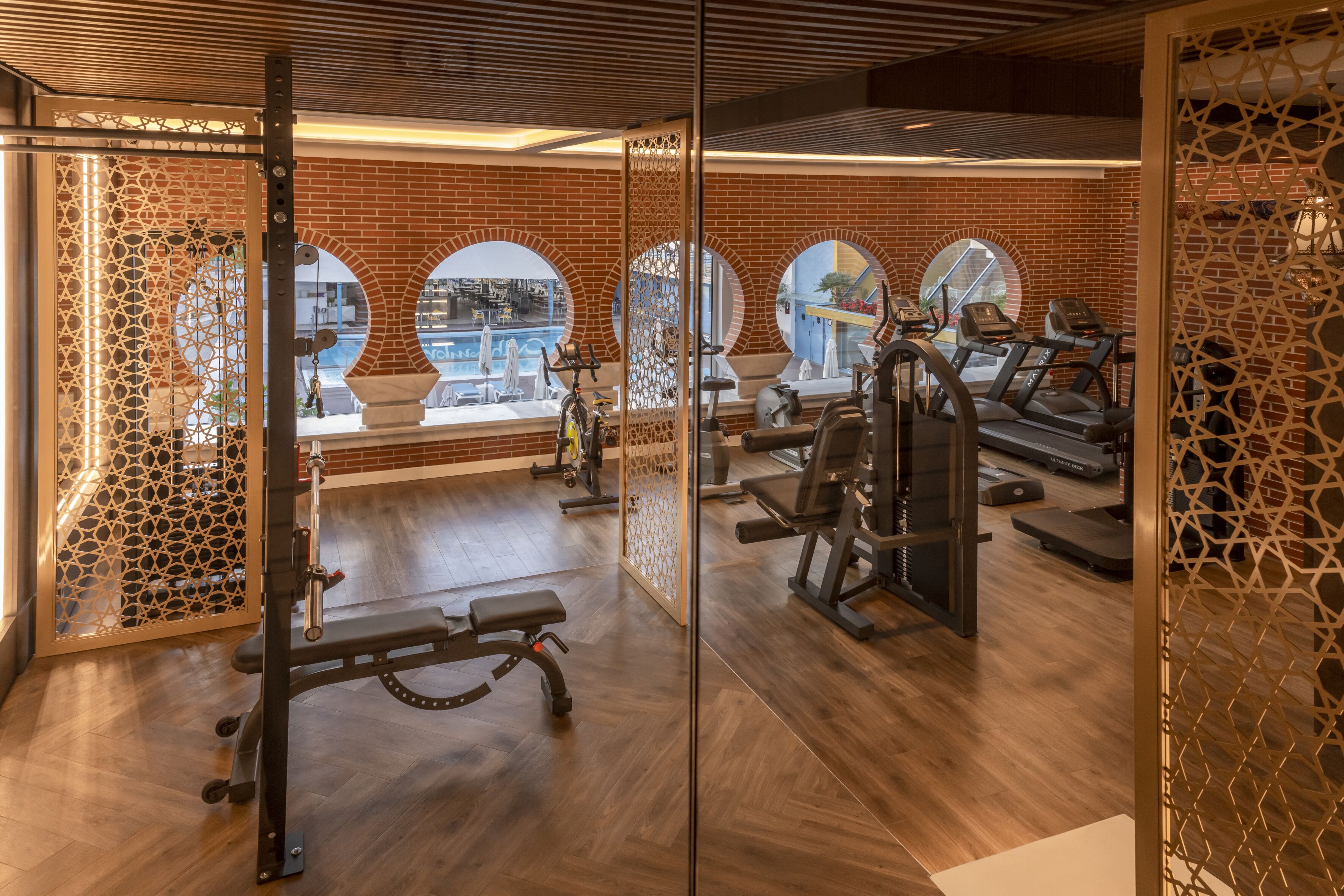 A gym with exercise equipment, wooden floors, and large windows with views of the city.