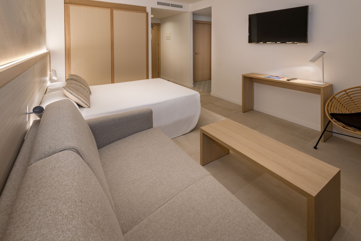 A modern hotel room with a bed, a sofa, a desk, and a TV.