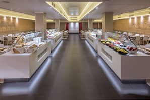 Um saguão de hotel moderno com uma passagem central, balcões de buffet e áreas de estar.