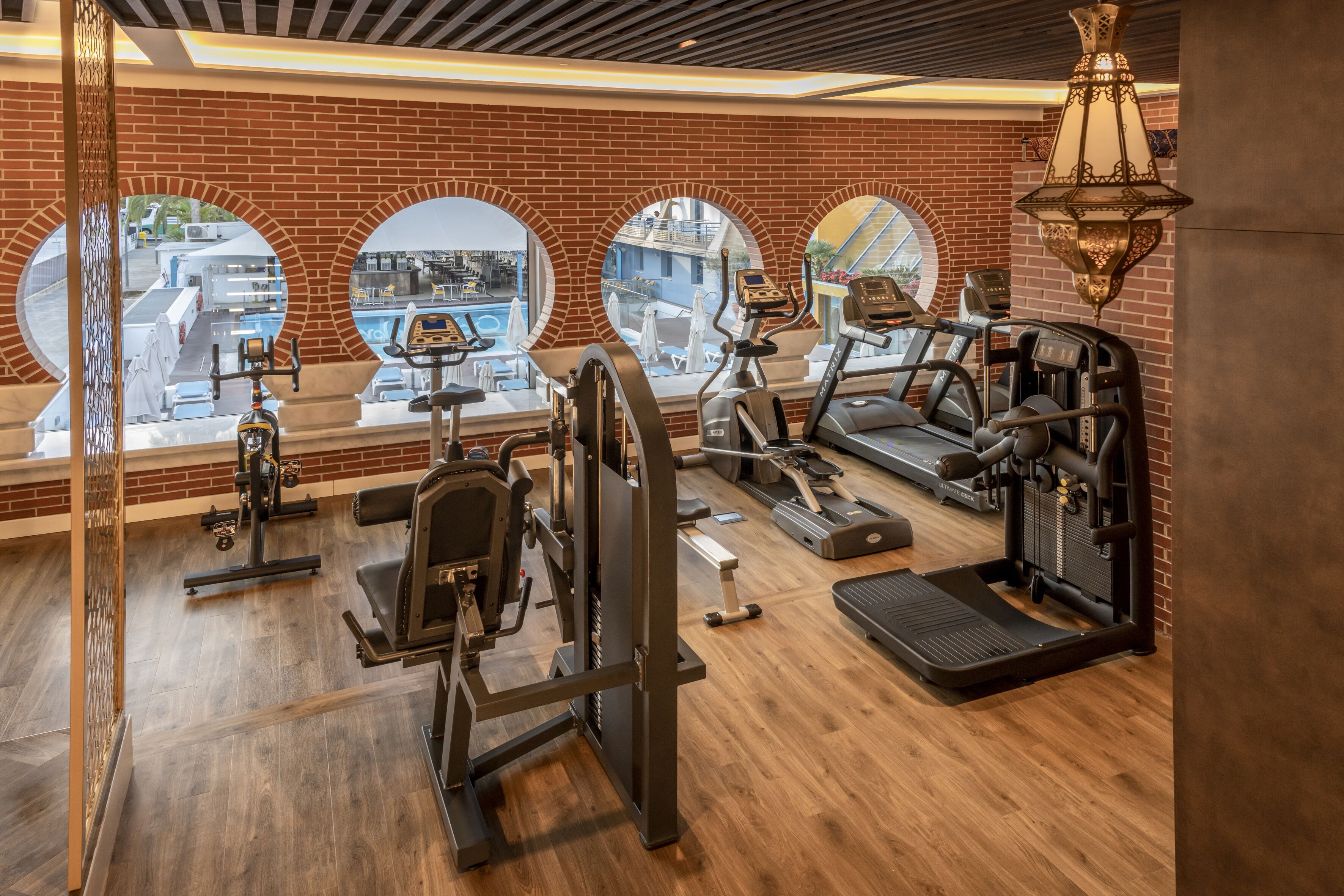 A gym with various exercise equipment, large windows, and a brick wall.
