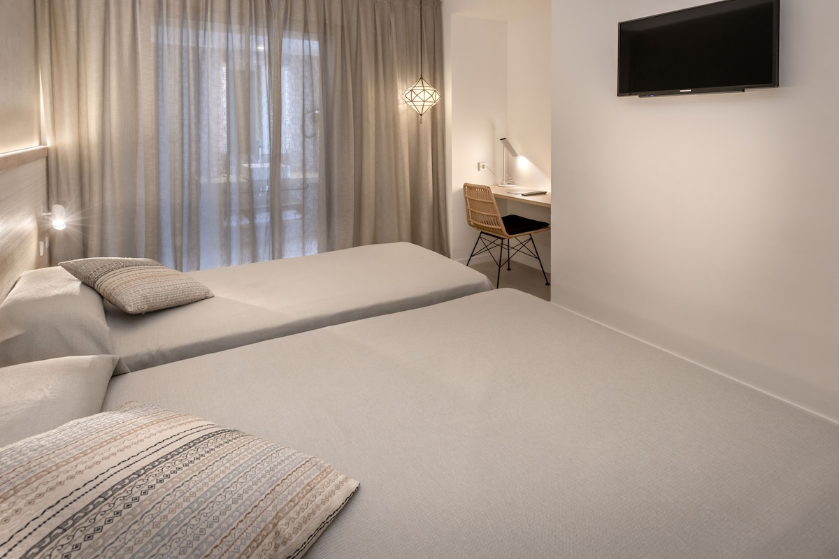 A modern hotel room with two beds, a desk, and a TV.