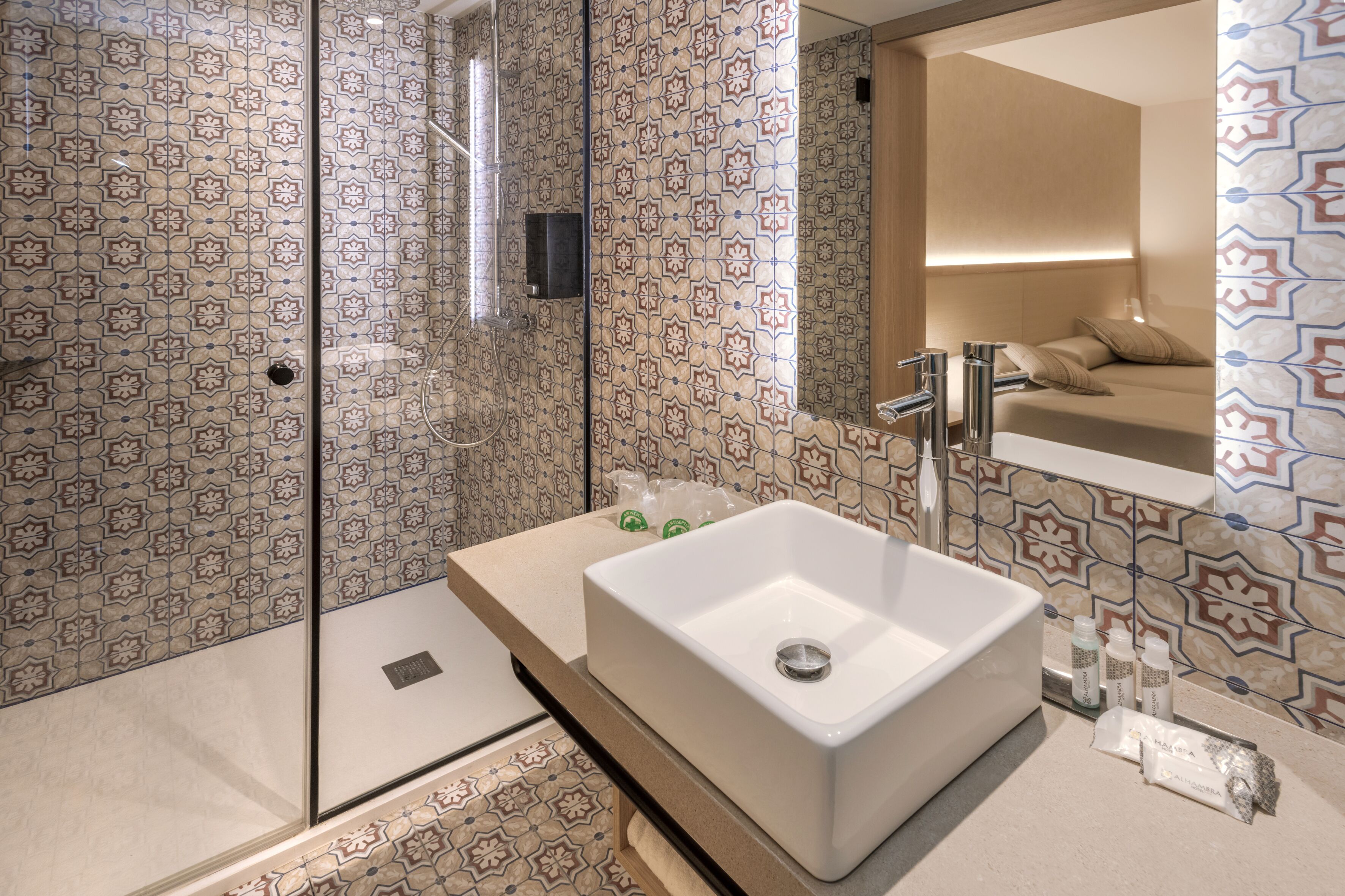 A modern bathroom with patterned tiles, a white sink, a glass shower enclosure, and a mirror above the sink.