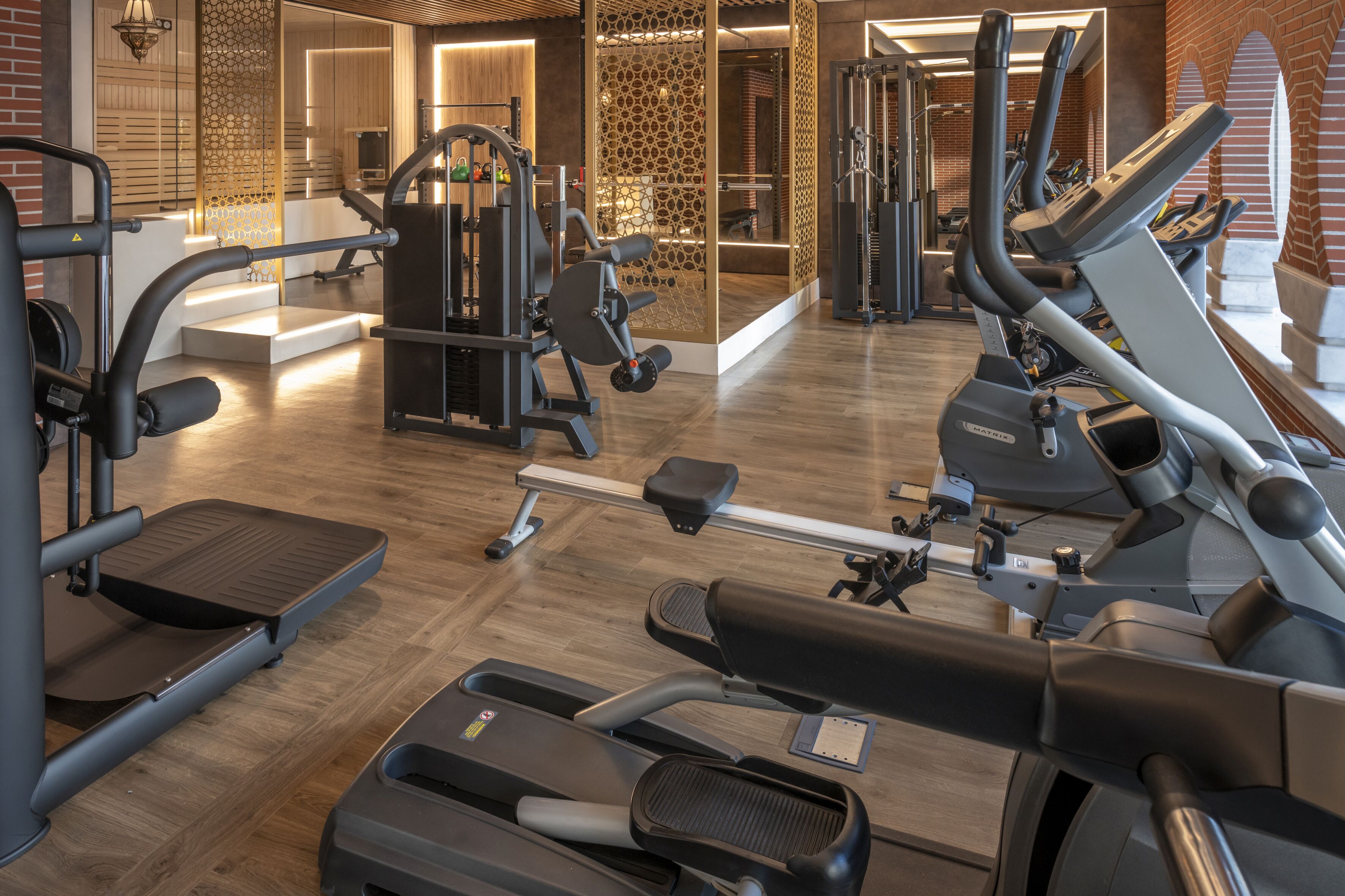 Un gimnasio con diverso equipo de ejercicio, incluyendo cintas de correr y máquinas de pesas, y piso de madera.