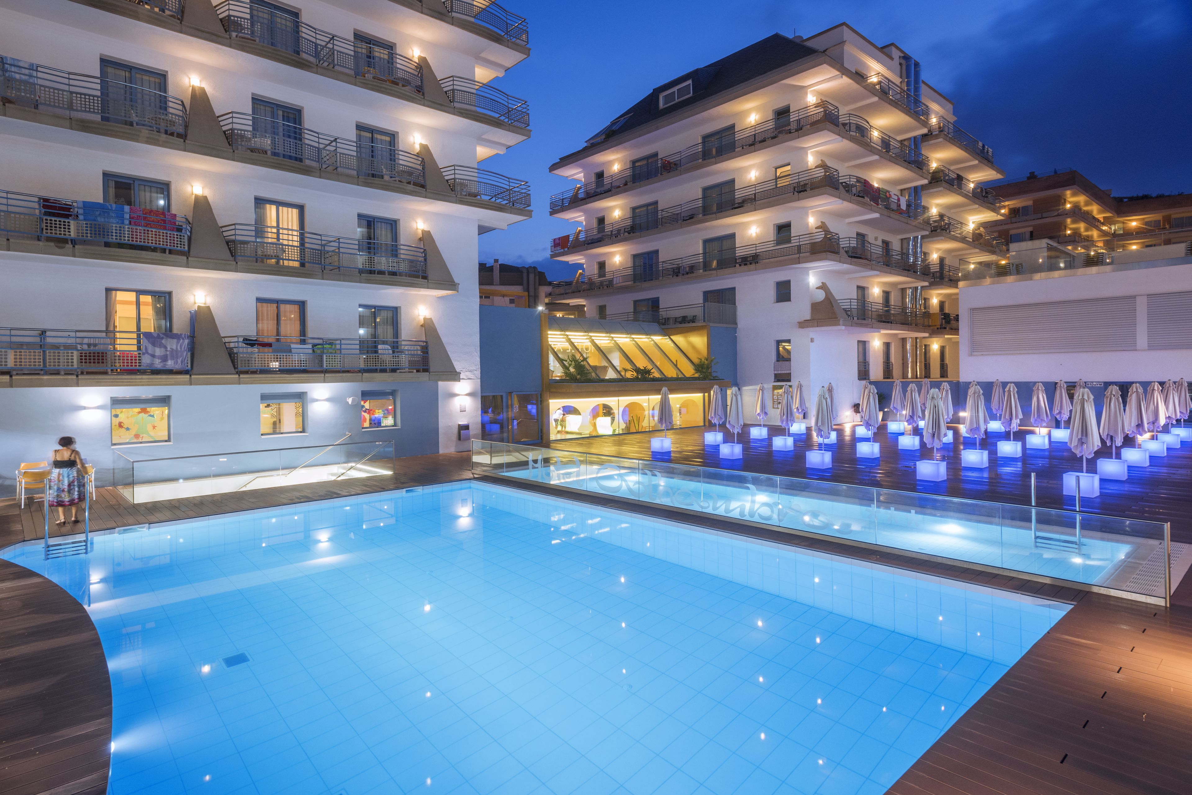Uma piscina interior ampla com um deck de madeira, rodeada por edifícios com vários andares, varandas e áreas de estar ao ar livre.
