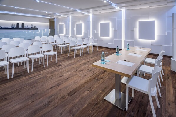 A conference room with white chairs and a long table, wooden flooring, and illuminated wall panels. - Hotel Alhambra (Santa Susanna)