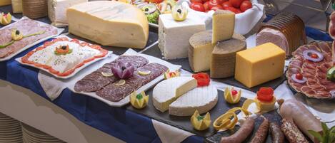 Un assortiment de fromages, de charcuteries et de salades est présenté sur une table de buffet.