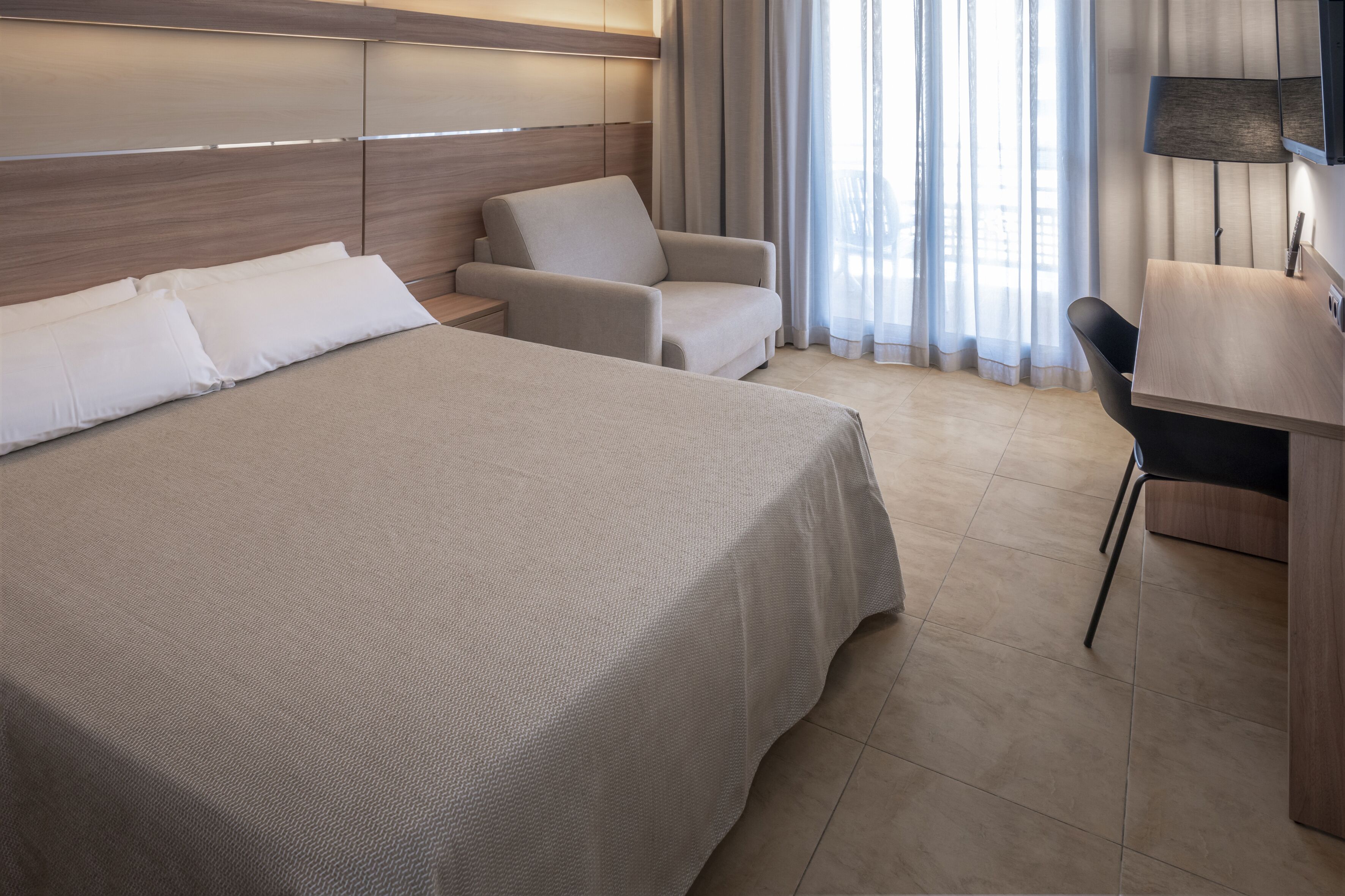 A hotel room with a large bed, a desk, a chair, and a sofa.