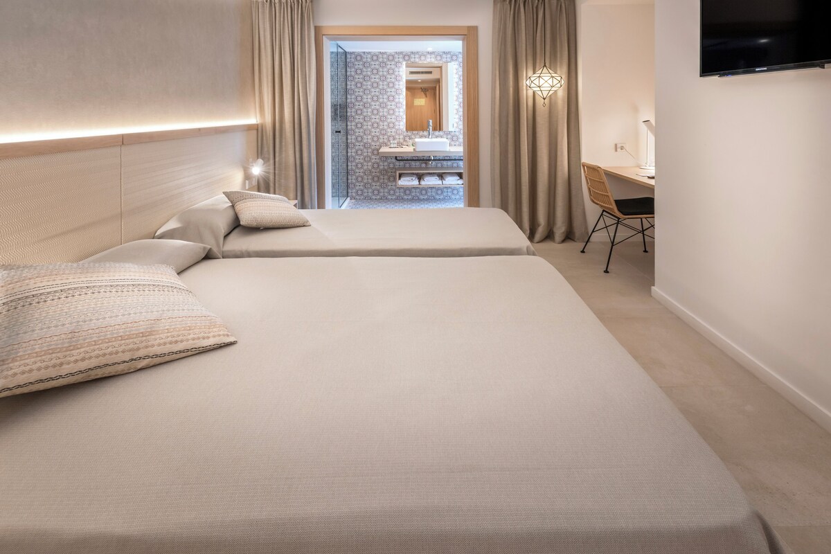 A hotel room with two beds, a desk, and a TV.