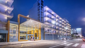 Un hôtel moderne doté d’une façade en verre, de nombreux balcons et d’une entrée bien éclairée.