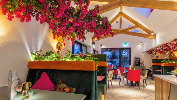 A restaurant interior with wooden beams, green upholstered seating, and vibrant pink flowers. - Wainstones Hotel (Middlesbrough)