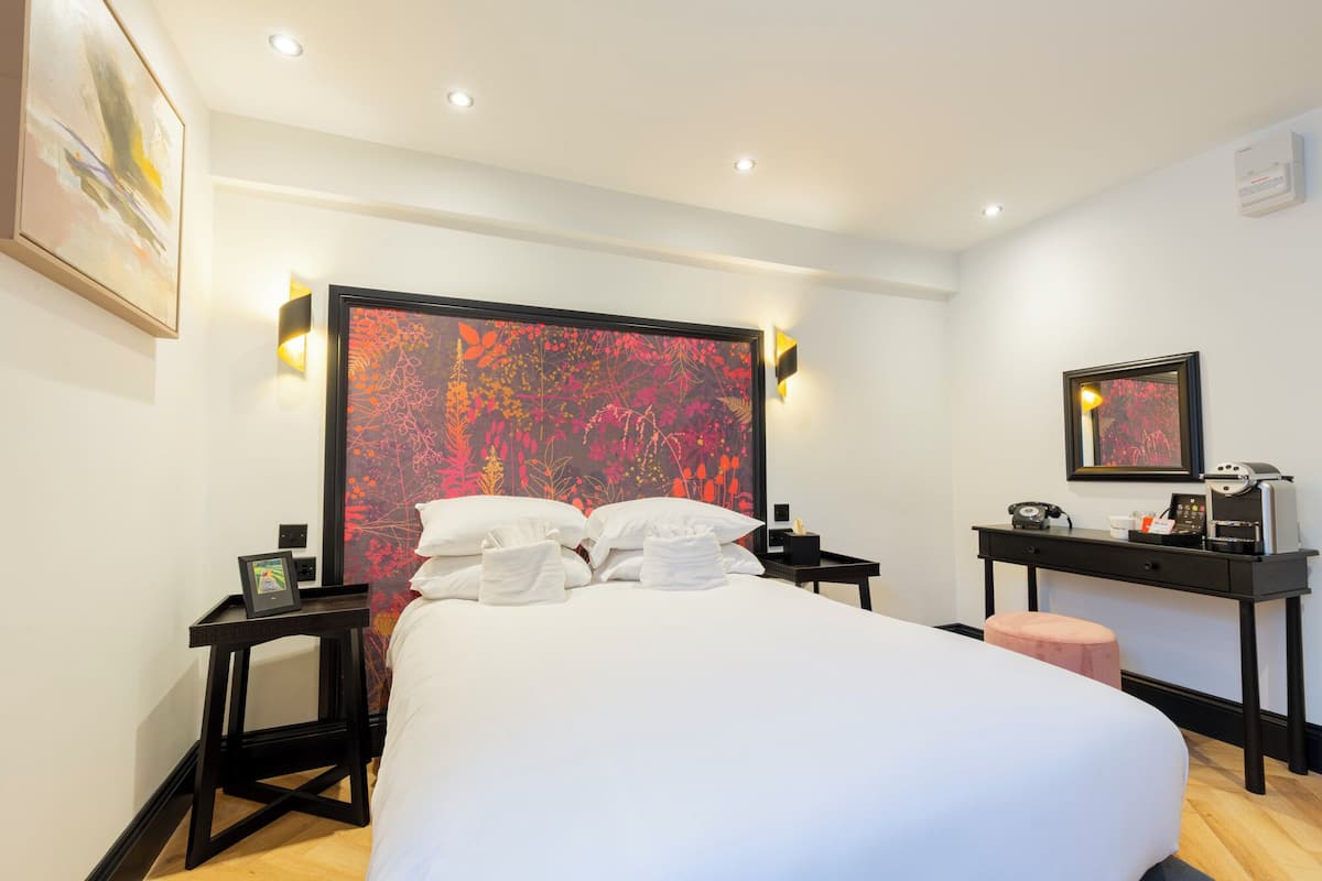 Ett hotellrum med en stor säng, ett skrivbord med en telefon och en kaffemaskin samt en spegel som är monterad på väggen.