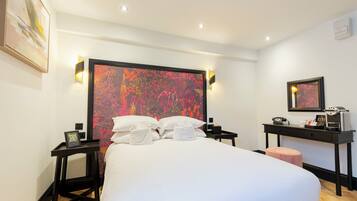 Hotelkamer met een groot bed, een bureau met telefoon en koffieapparaat, en een spiegel aan de muur.