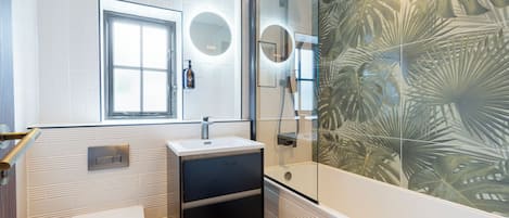 Un baño moderno con inodoro, lavabo y ducha. Hay una ventana sobre el inodoro y un motivo decorativo de hojas en la pared.