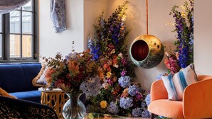 A living room with a blue sofa, an orange armchair, and a variety of colorful flowers in vases. - Wainstones Hotel (Middlesbrough)