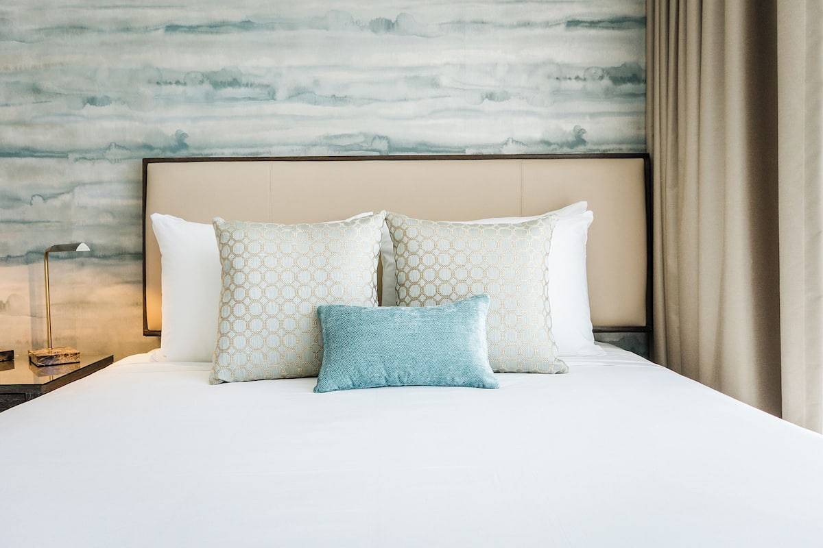 A neatly made bed with patterned pillows and a headboard against a textured wall.