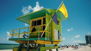 Una torre de salvavidas en la playa de Miami, con un cielo azul despejado y el océano al fondo.