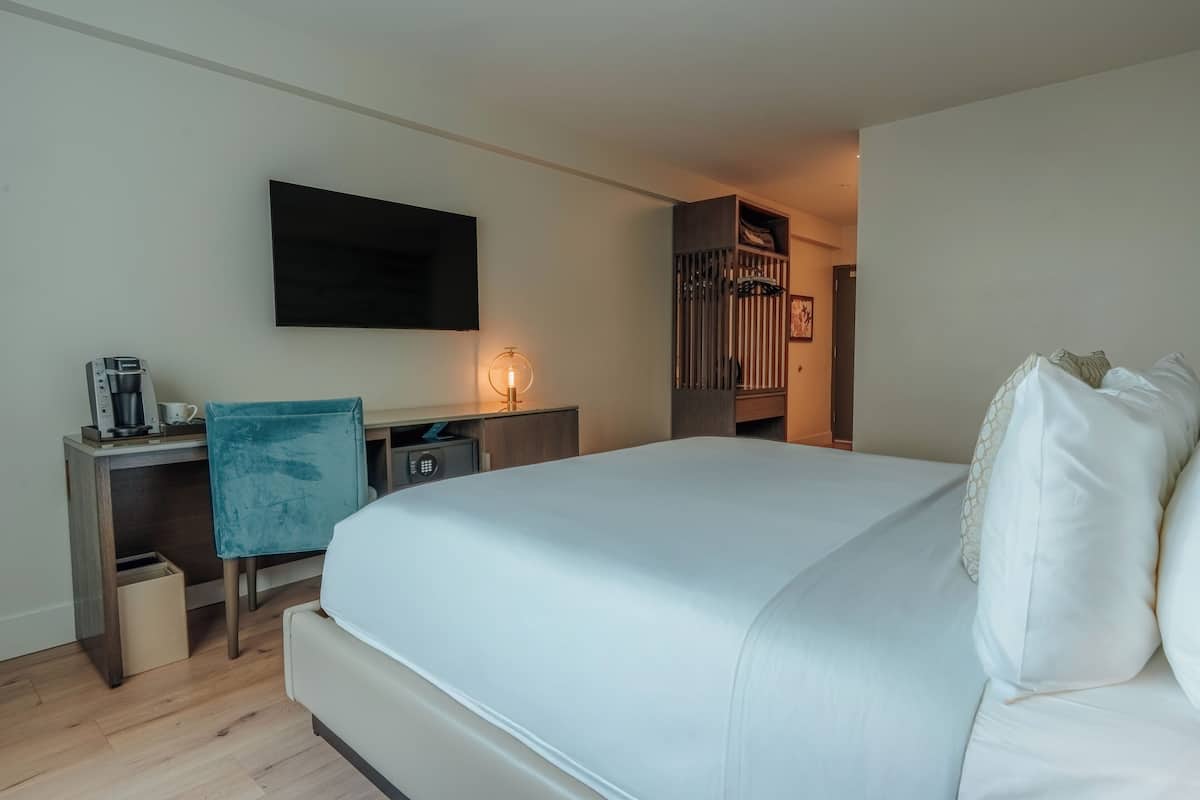 A hotel room with a bed, a desk with a chair, a coffee maker, a TV, and a wardrobe.