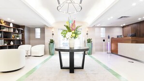 Un área de recepción con una mesa redonda, sillas blancas, una estantería y un jarrón decorativo con flores.
