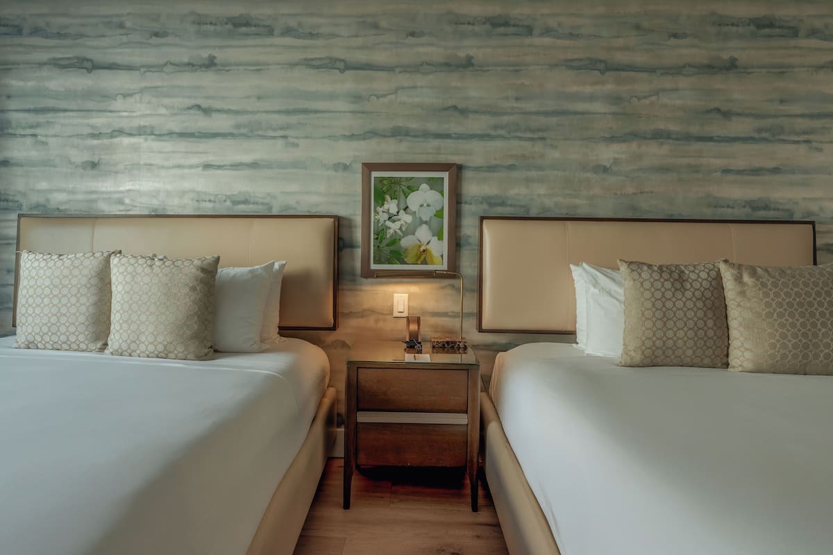 A hotel room with two beds, a nightstand, a framed floral artwork, and a textured wall.