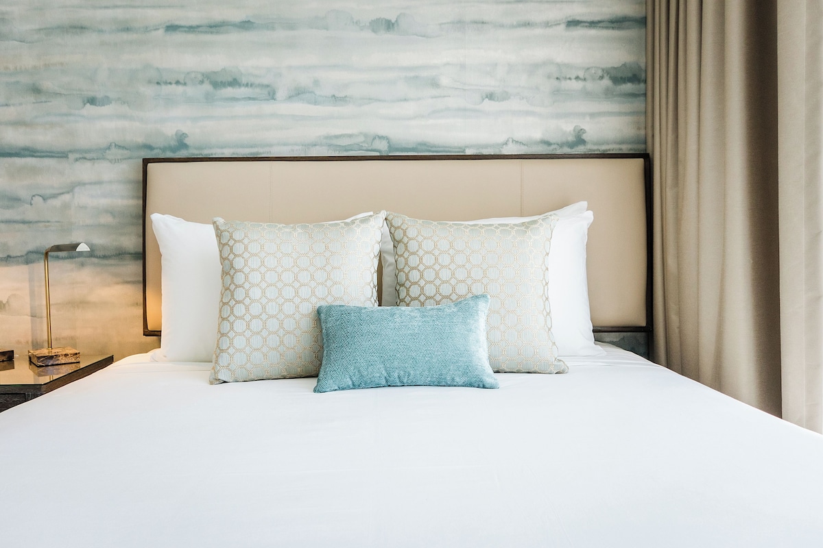 A neatly made bed with patterned pillows and a headboard against a textured wall.