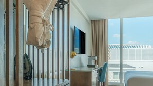 Habitación de hotel con armario de madera, escritorio, silla, cama y ventana grande con vista a la ciudad.