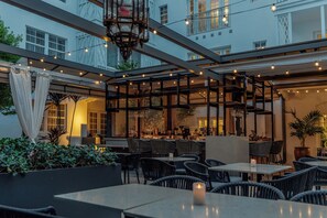 An outdoor dining area with tables and chairs, string lights, and a view of the building's interior. - Iberostar Waves Miami Beach (Miami Beach)