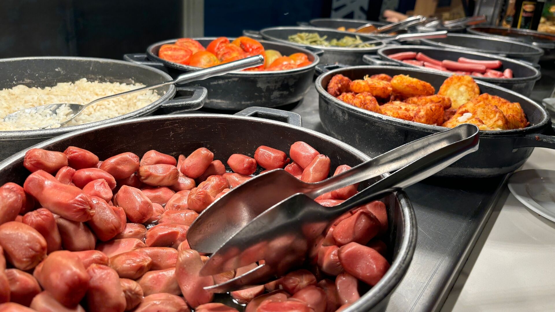 Un bufé con diversas opciones de comida, incluyendo salchichas, arroz y verduras.