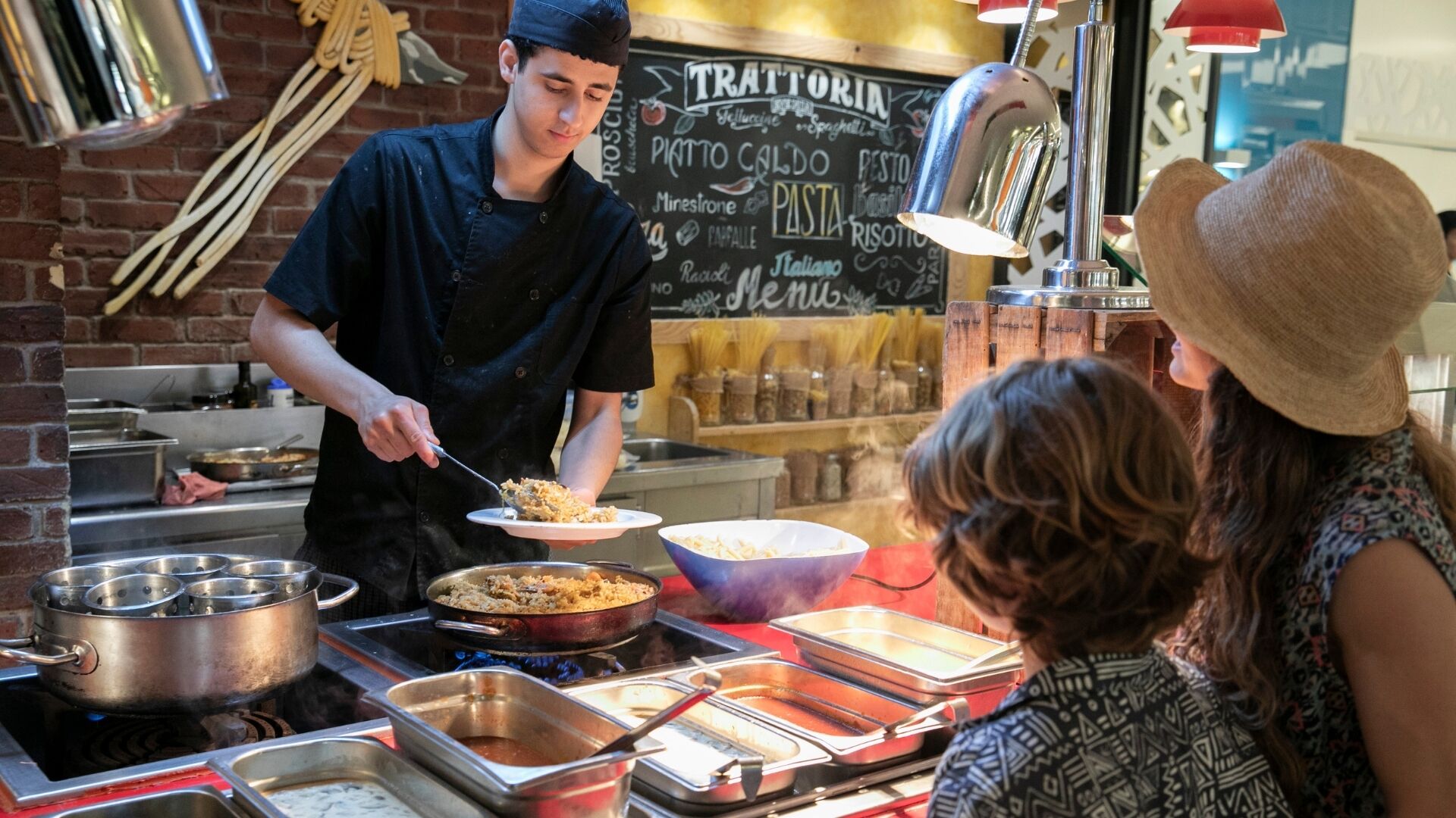 Una persona sirviendo comida en un mostrador con diversos platos y utensilios de cocina.