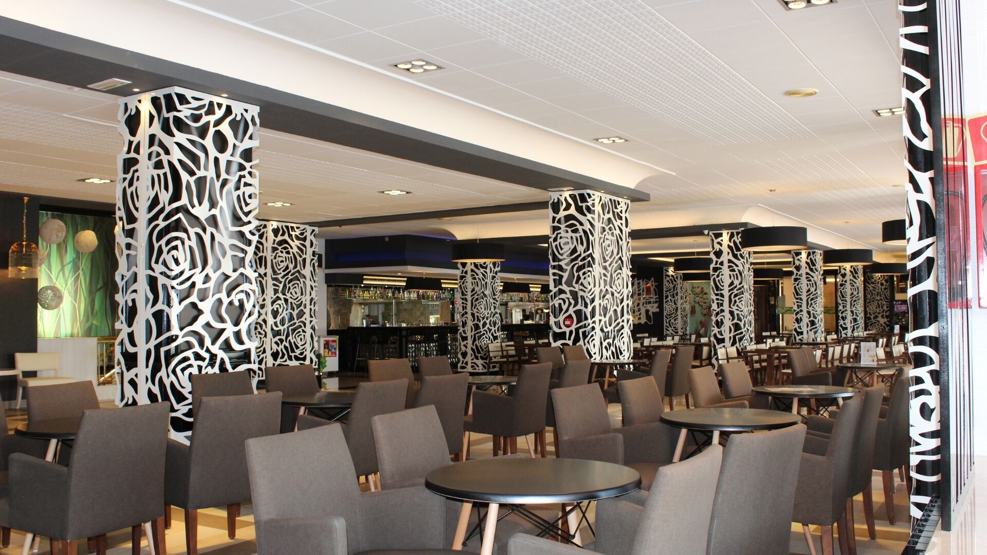 Un interior moderno con techos altos, columnas con diseño y una zona de bar al fondo.