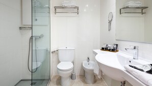 A modern bathroom with a glass-enclosed shower, a toilet, a bidet, and a sink with a mirror.