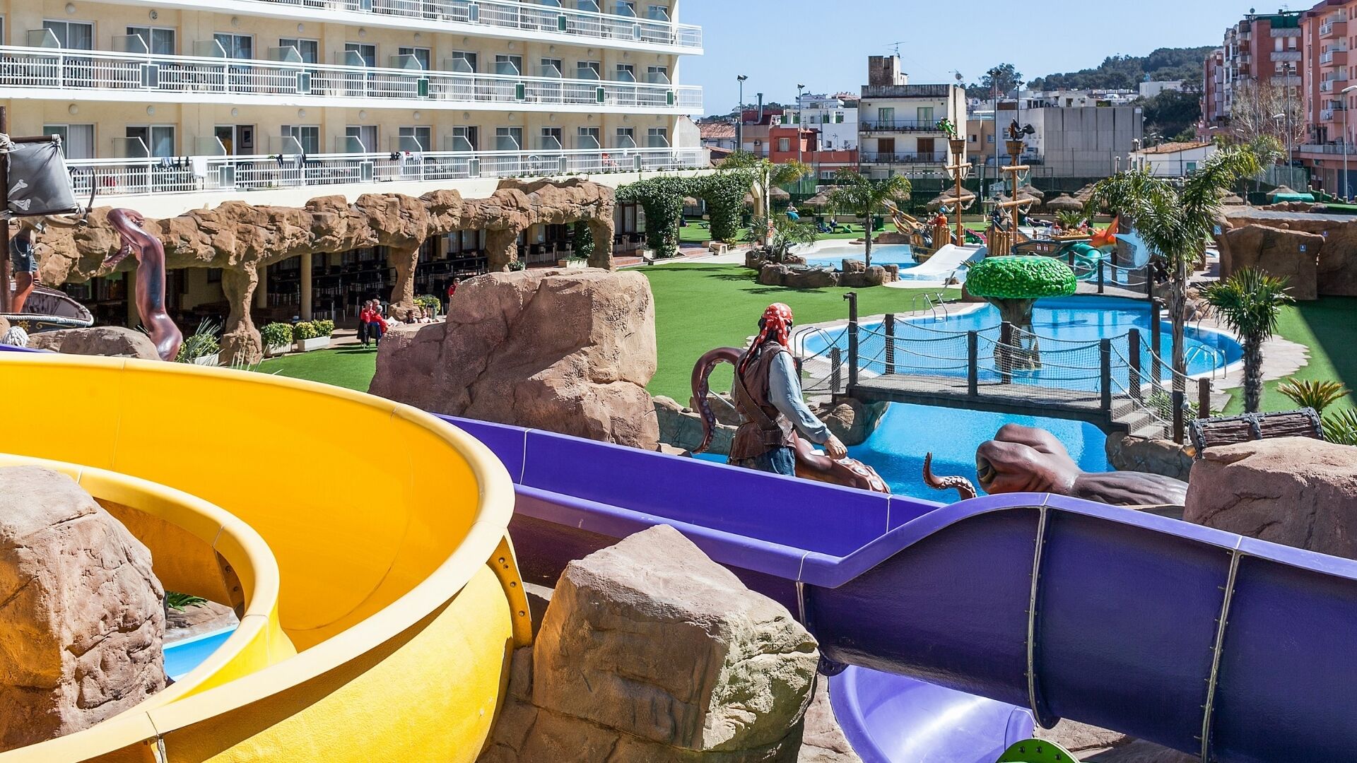 Een waterpark met glijbanen, een zwembad en een gebouw met balkons in de verte.