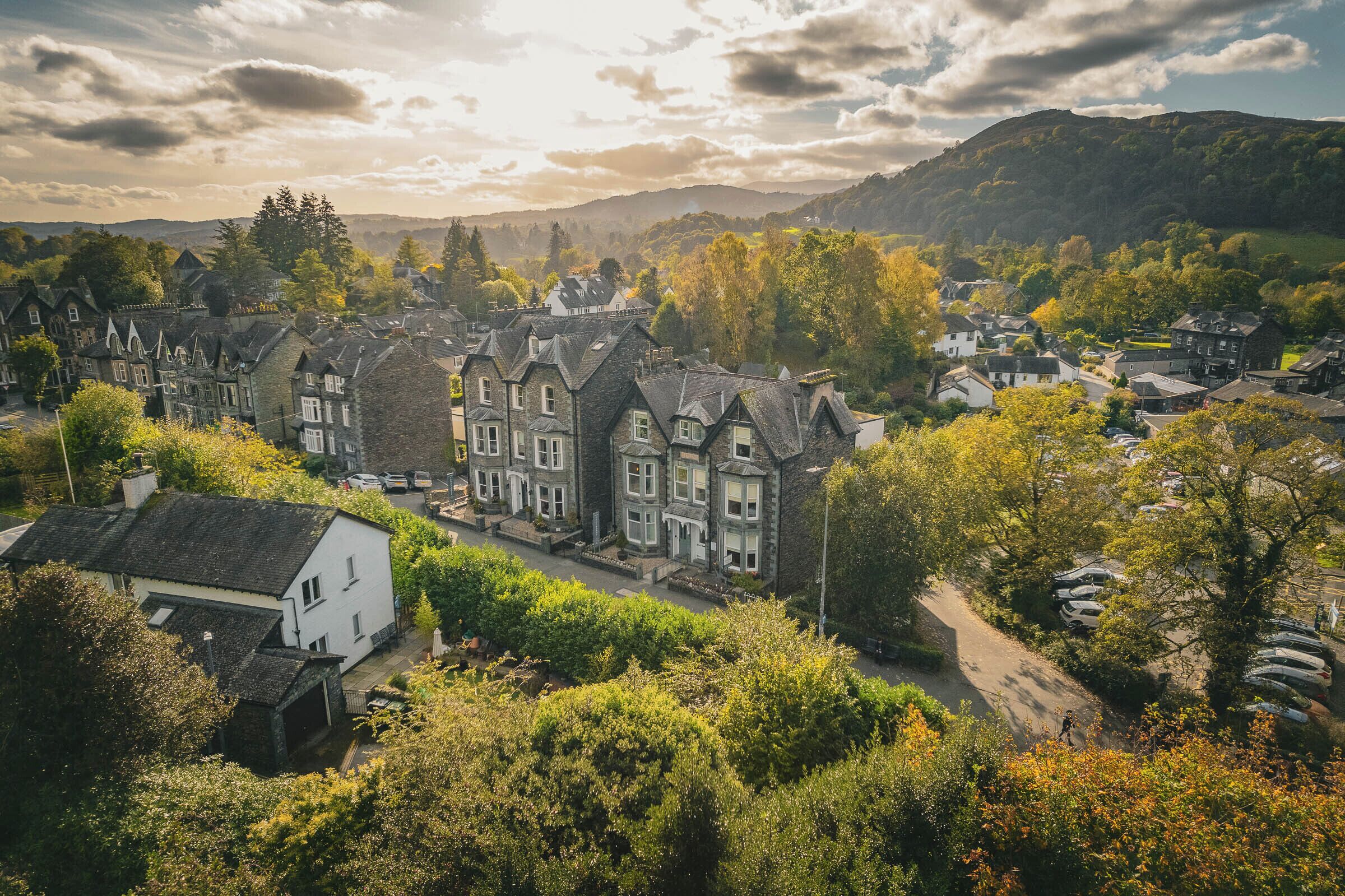 A village with traditional stone houses, a main road, and a parking area.