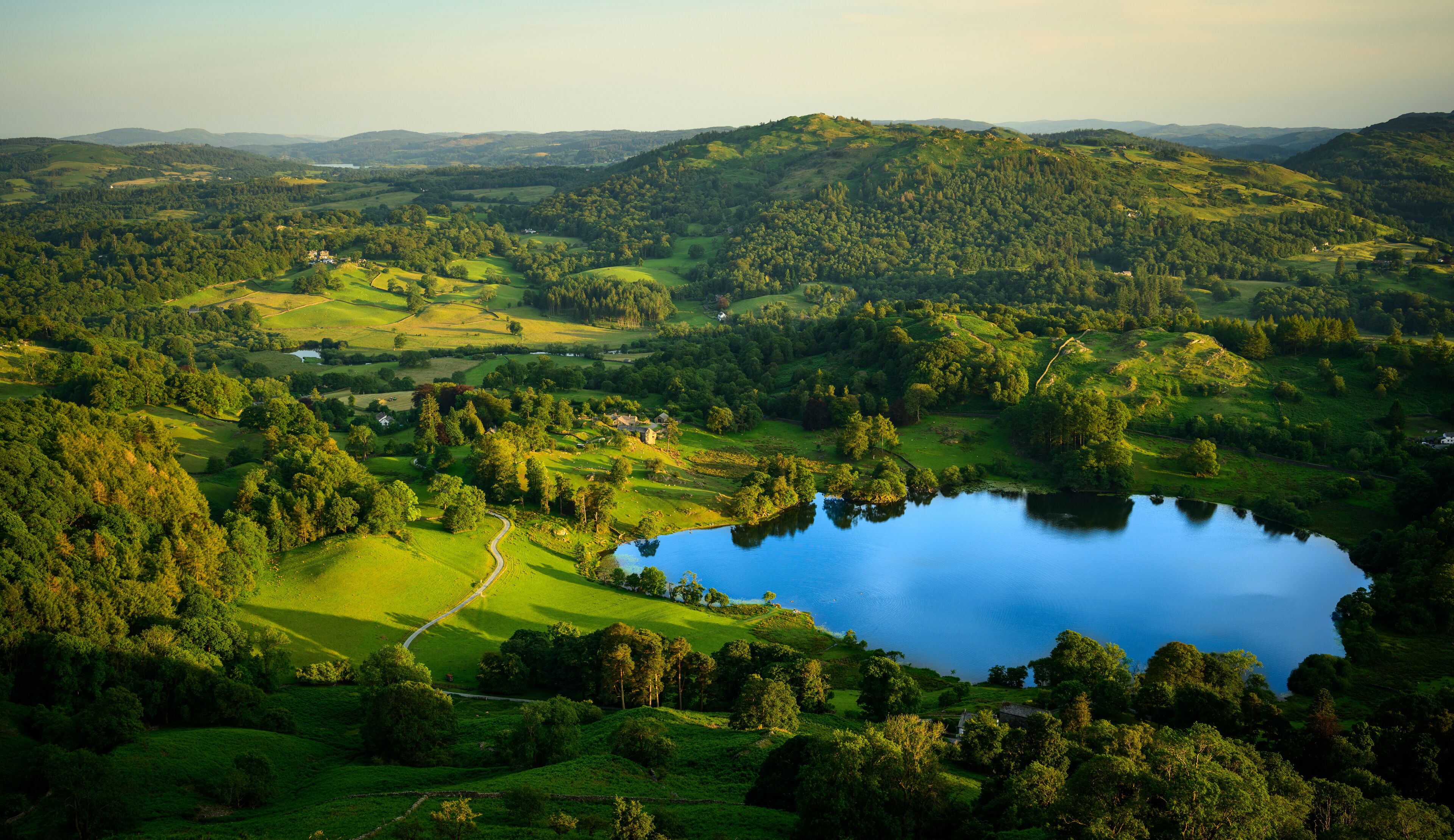 A panoramic view of a lush green landscape with rolling hills, a lake, and scattered buildings.