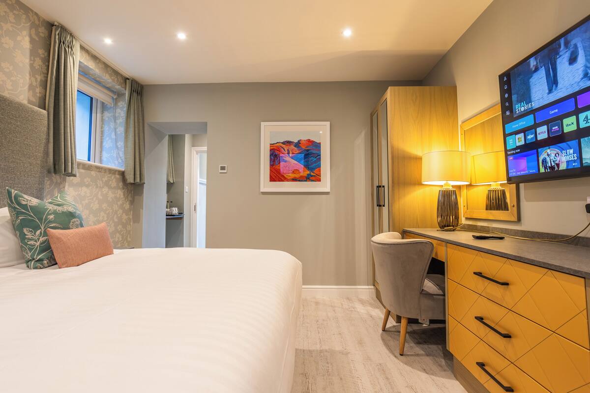 A hotel room with a bed, a desk, a chair, a TV, and a framed picture on the wall.
