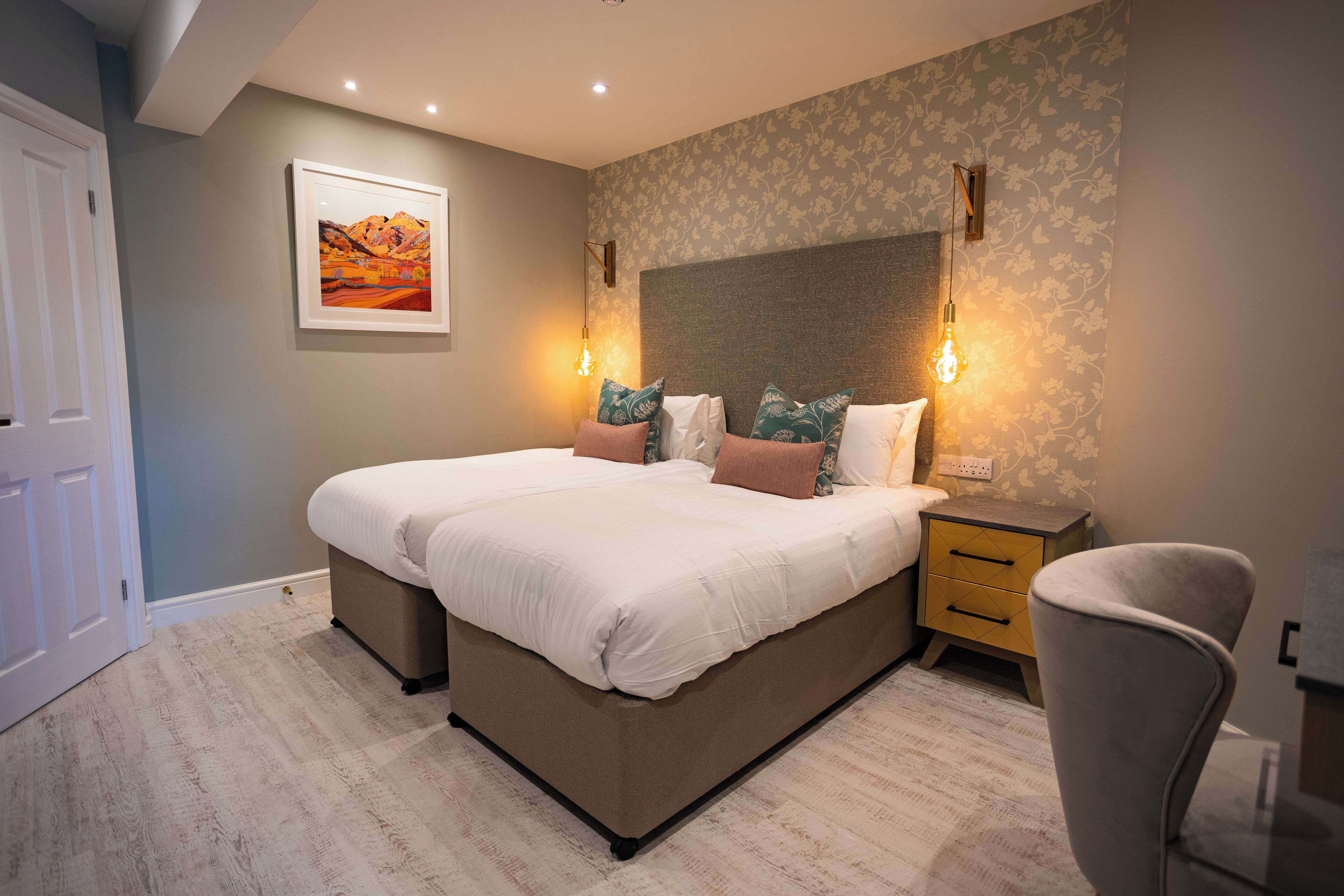 A bedroom with a large bed, bedside tables, a chair, and a wall-mounted light fixture.