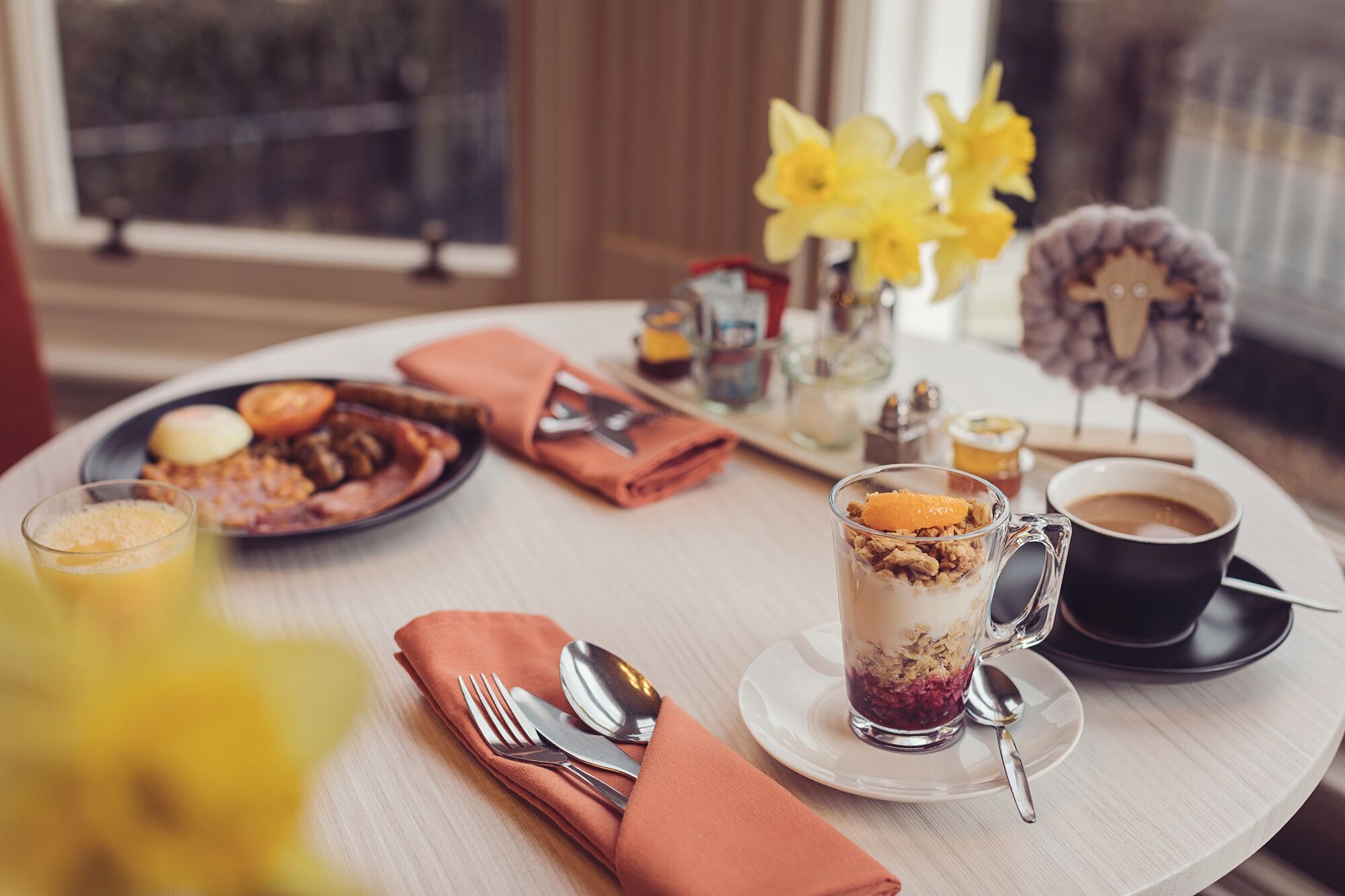 Una colazione: un piatto di cibo, un bicchiere di succo d'arancia, una tazza di caffè e un vaso decorativo con fiori.