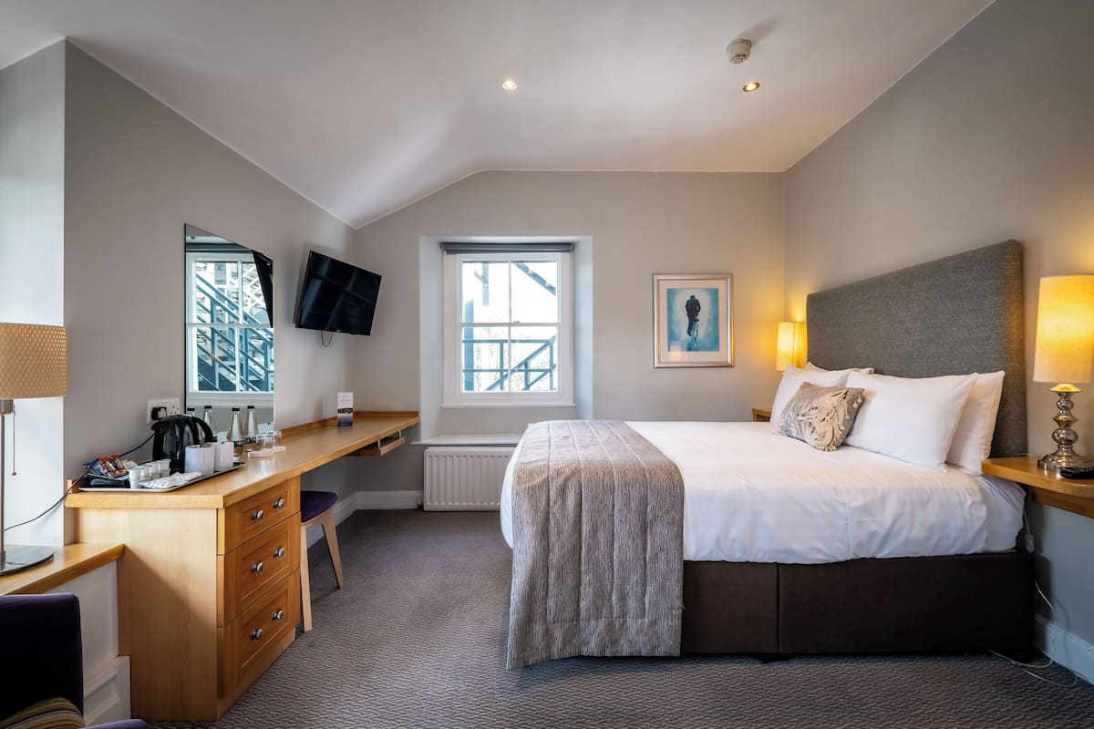 A hotel room with a bed, desk, chair, and a window with a view of a building.