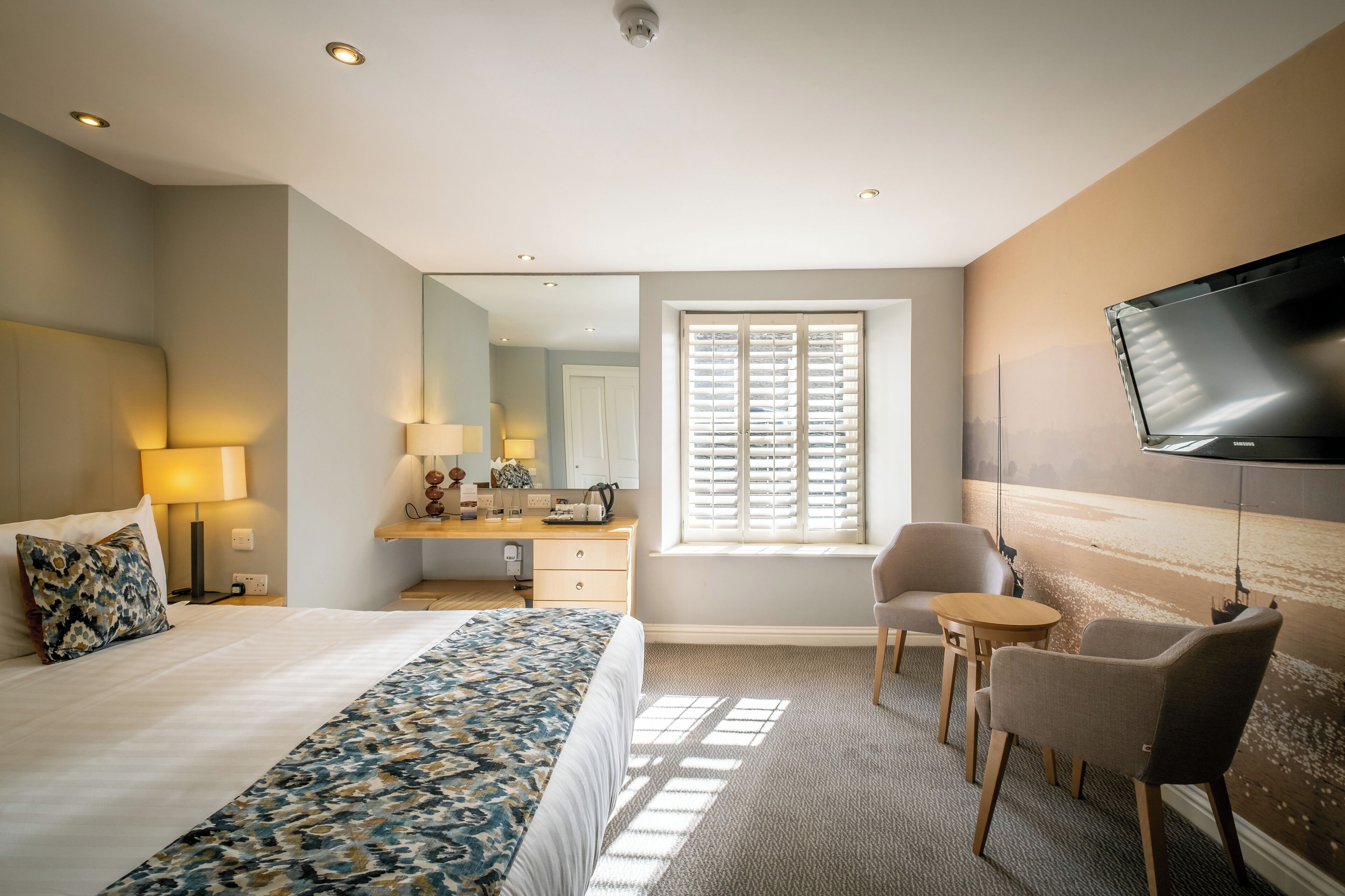 A hotel room with a bed, a desk, a chair, a television, and a window with blinds.