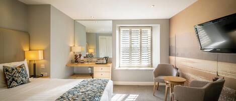 A hotel room with a bed, a desk, a chair, a television, and a window with blinds.