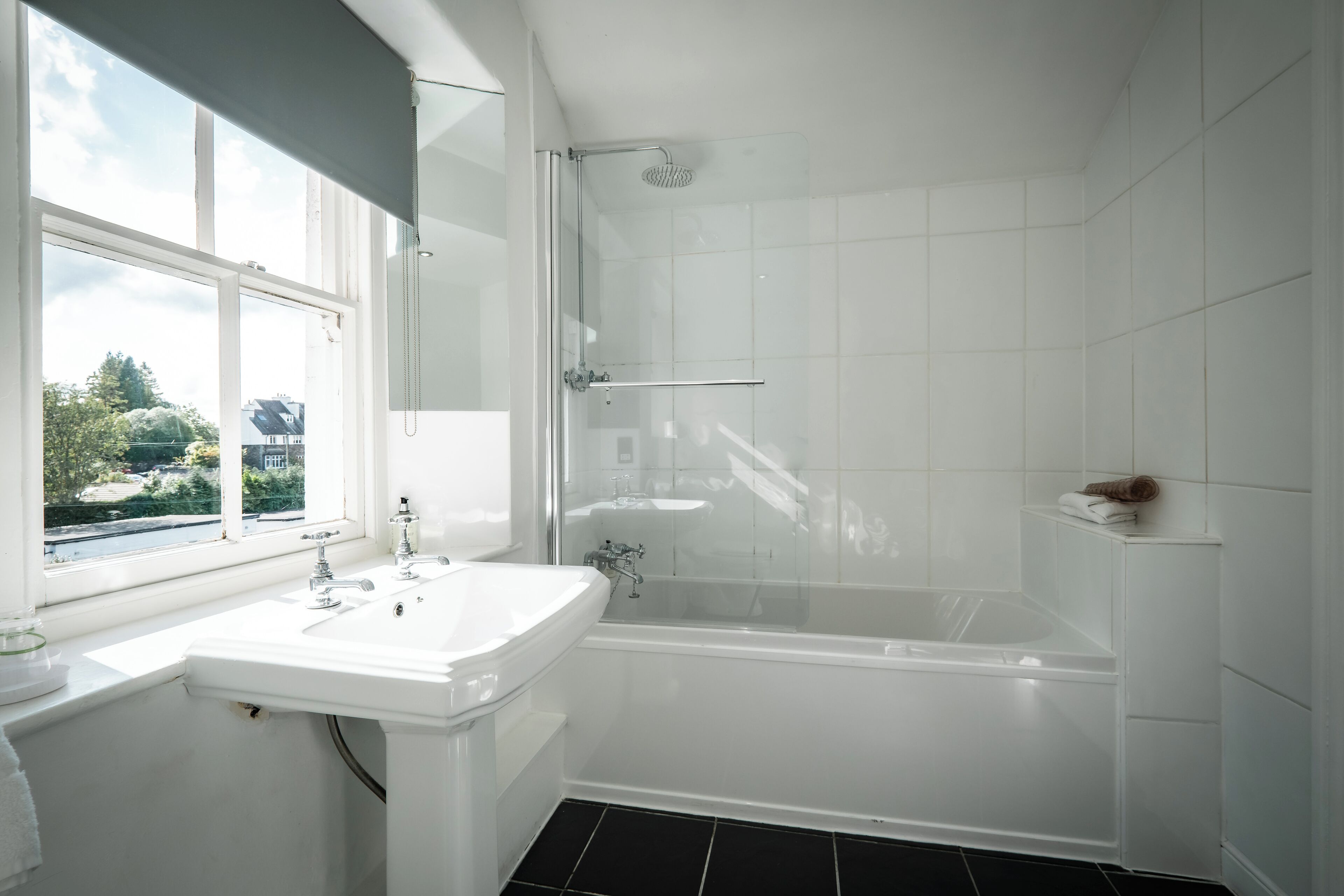 A modern bathroom with a large window, a bathtub, and a sink.